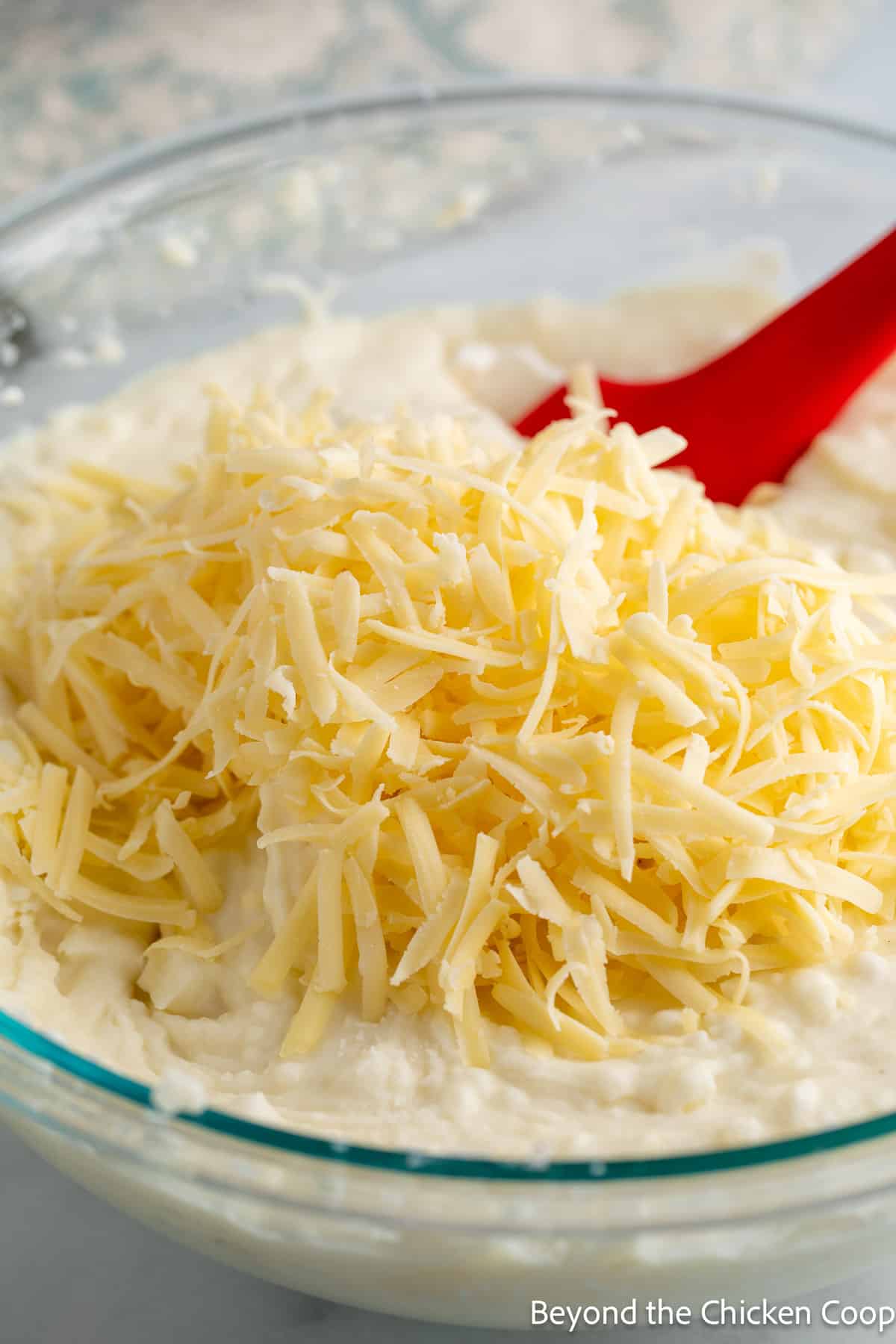 Adding shredded cheese to a bowl of mashed potatoes. 