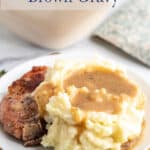 Mashed potatoes with gravy next to a pork chop on a plate.