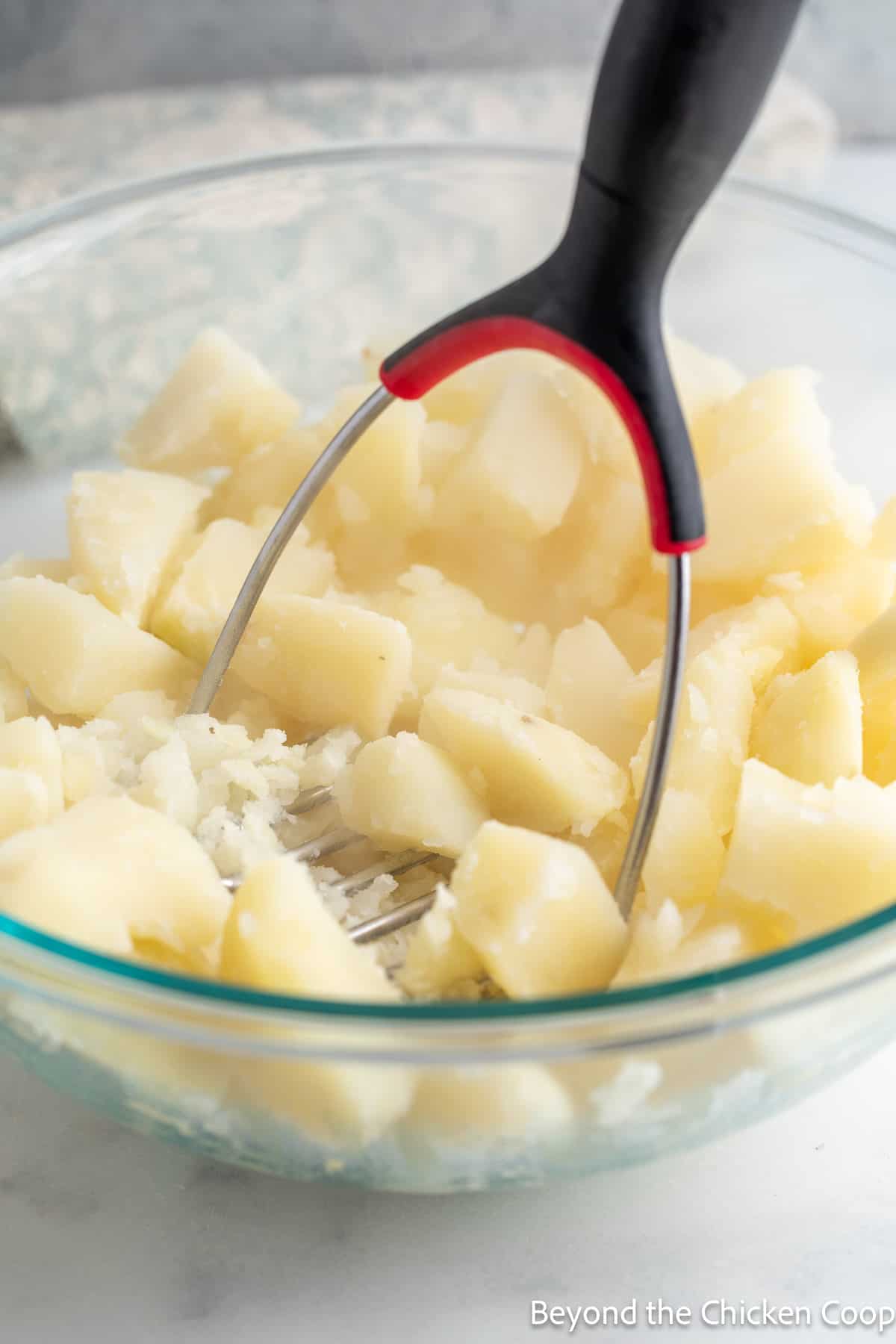 Mashing cooked potatoes in a glass bowl. 