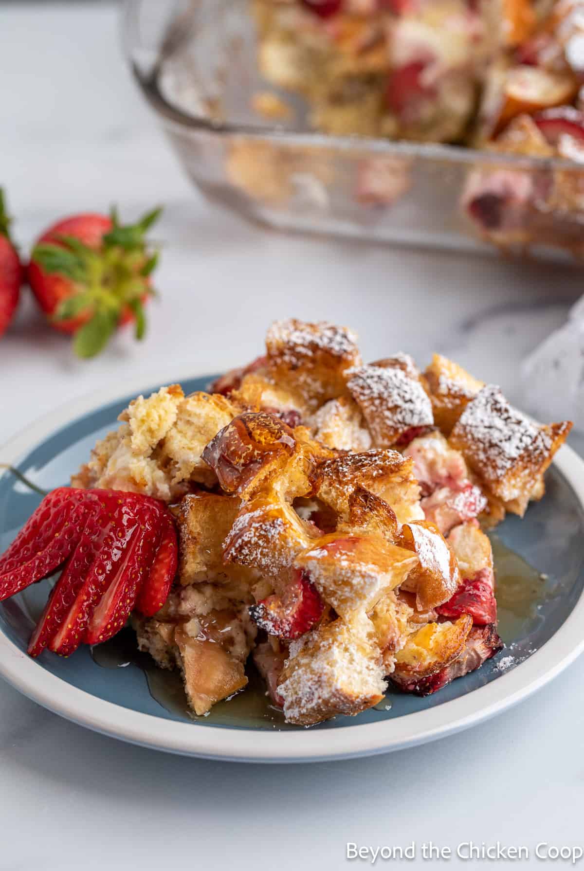 A plate filled with a baked French toast and strawberries. 