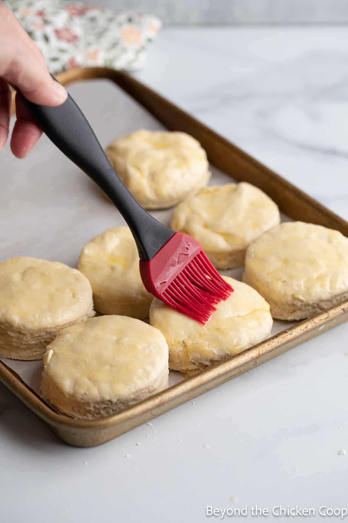Brushing butter on top of unbaked biscuits. 