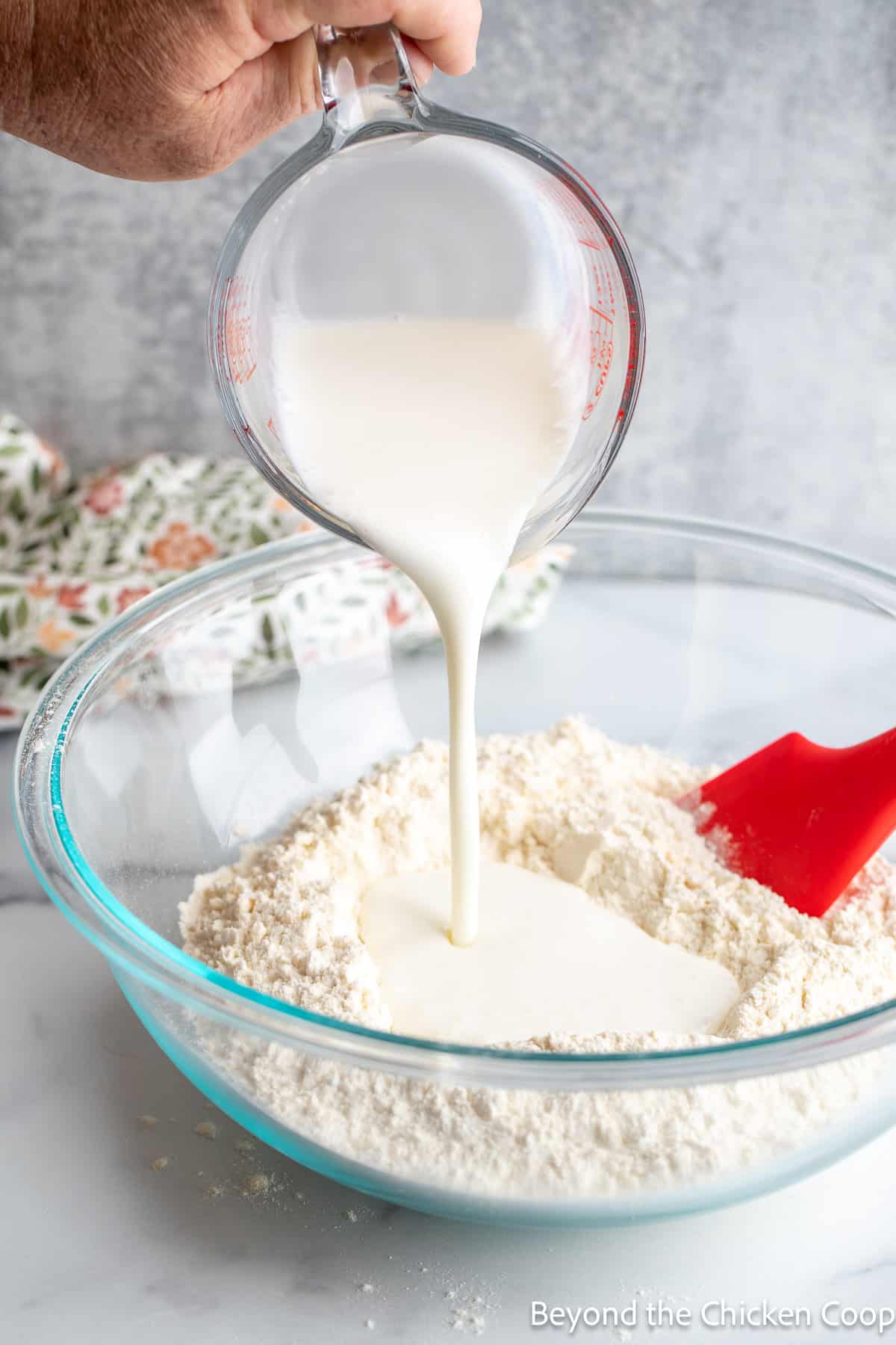 Pouring buttermilk into a bowl full of flour. 