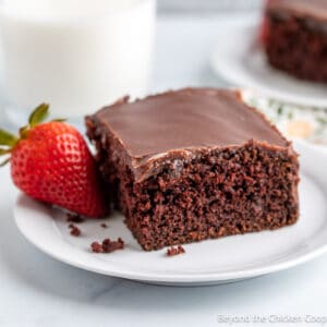 A slice of chocolate cake on a white plate with a strawberry.