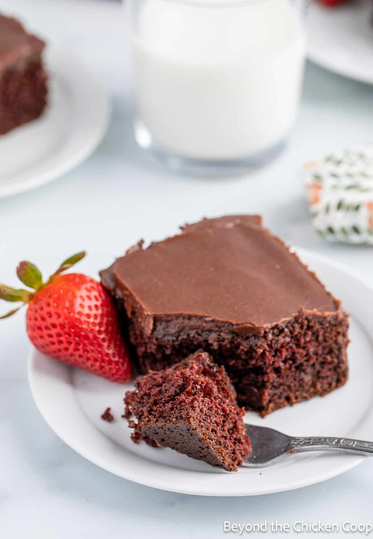 A white plate with chocolate cake with a smooth chocolate frosting. 