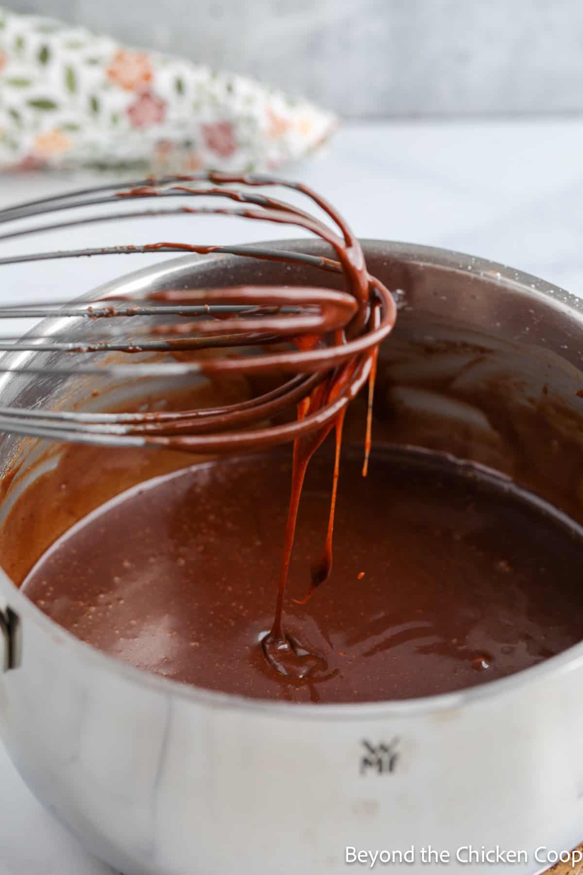A whisk dripping with chocolate icing. 