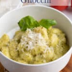 A bowl with gnocchi topped with parmesan cheese and a basil leaf.