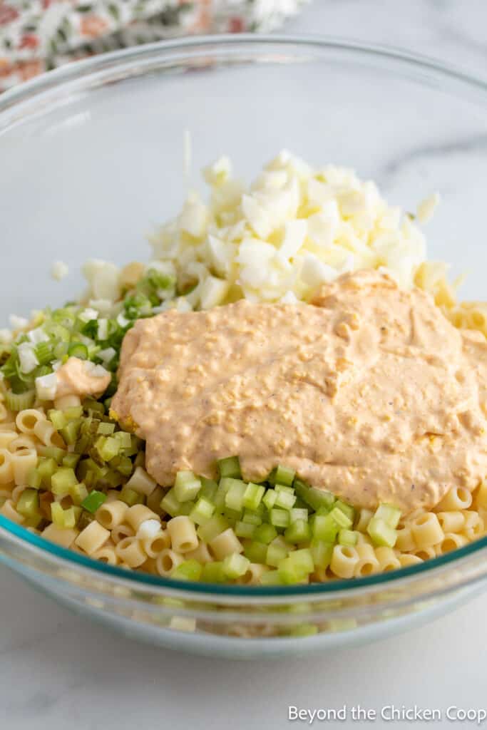 Mixing pasta with a dressing in a large glass bowl. 