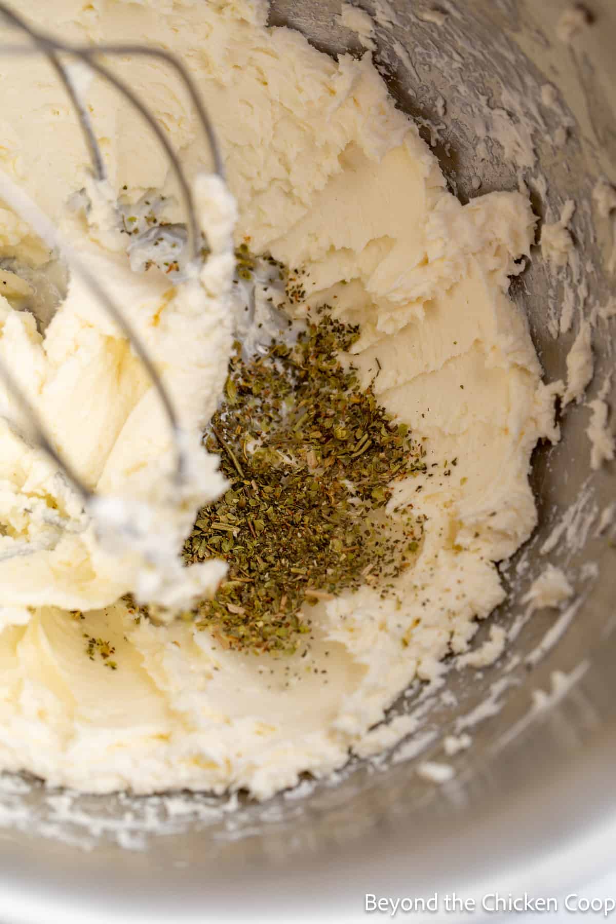 Cream cheese with dried herbs in a mixing bowl. 