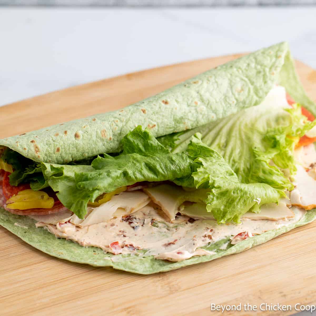 Rolling up a pinwheel in a green tortilla wrap. 