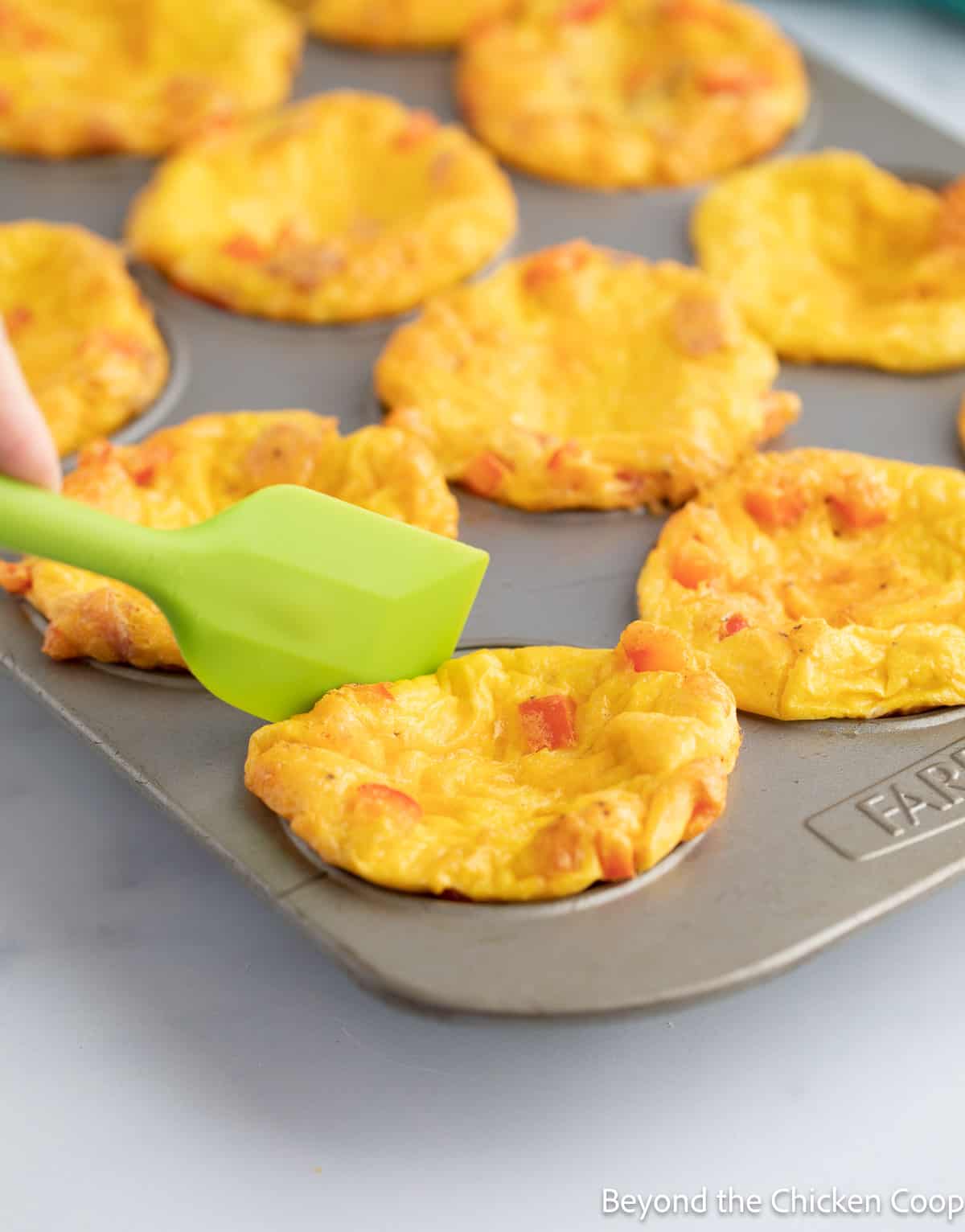 Using a green spatula to help release eggs from a muffin tin. 