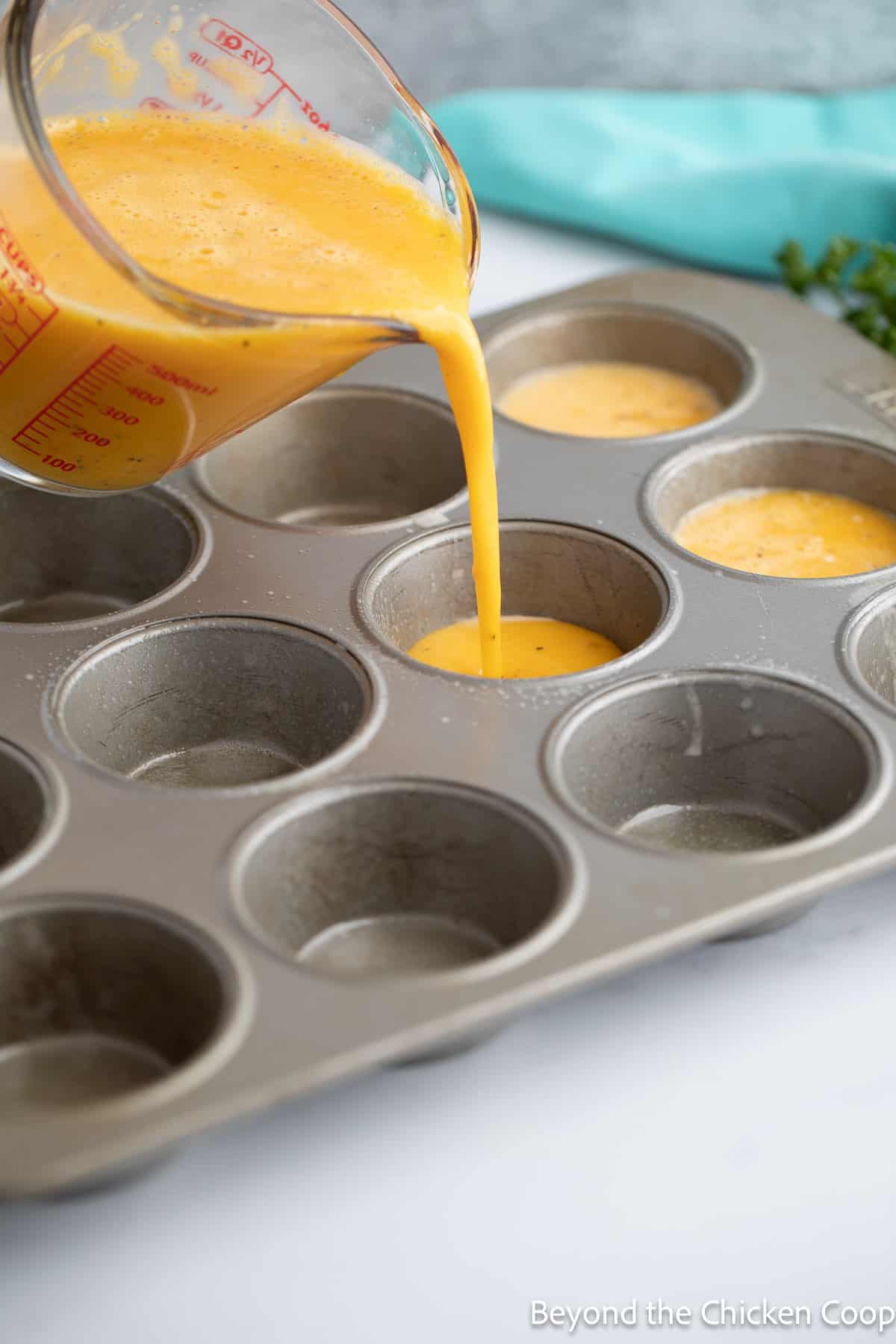 Pouring egg mixture into muffin tins. 
