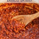 Baked beans in a large pot with a wooden spoon.