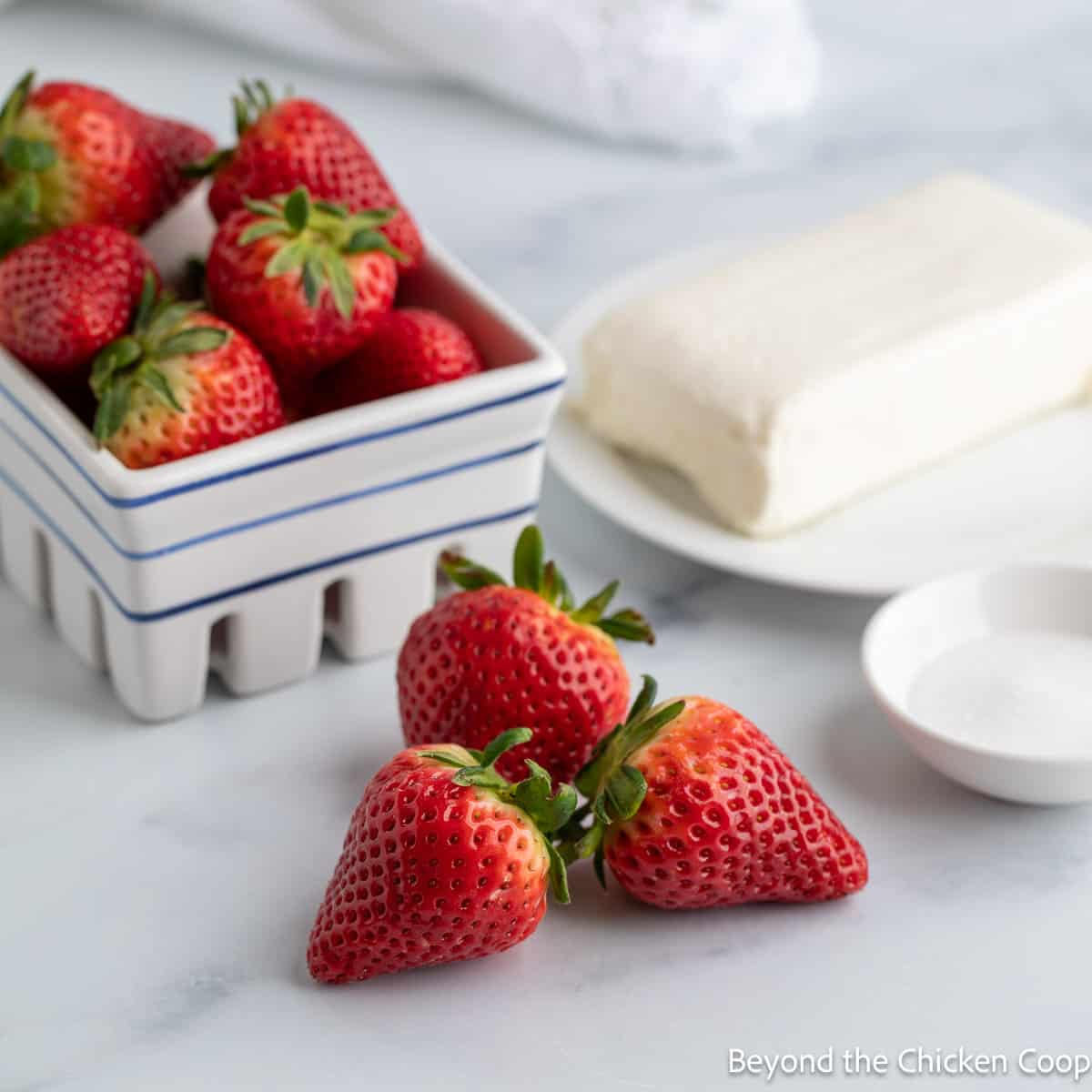 A basket with fresh strawberries next to a block of cream cheese. 