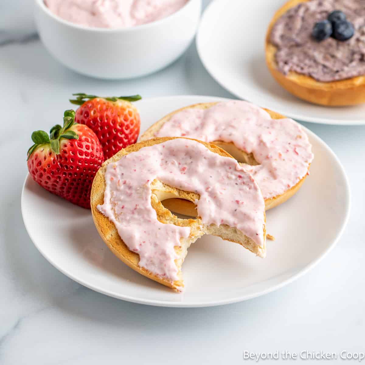 A bagel topped with a pink cream cheese. 