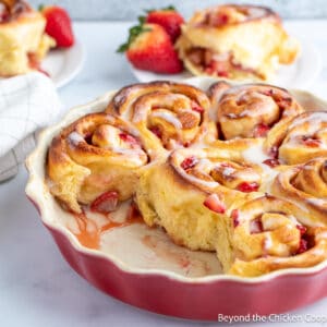 Cinnamon rolls filled with strawberries in a red dish.