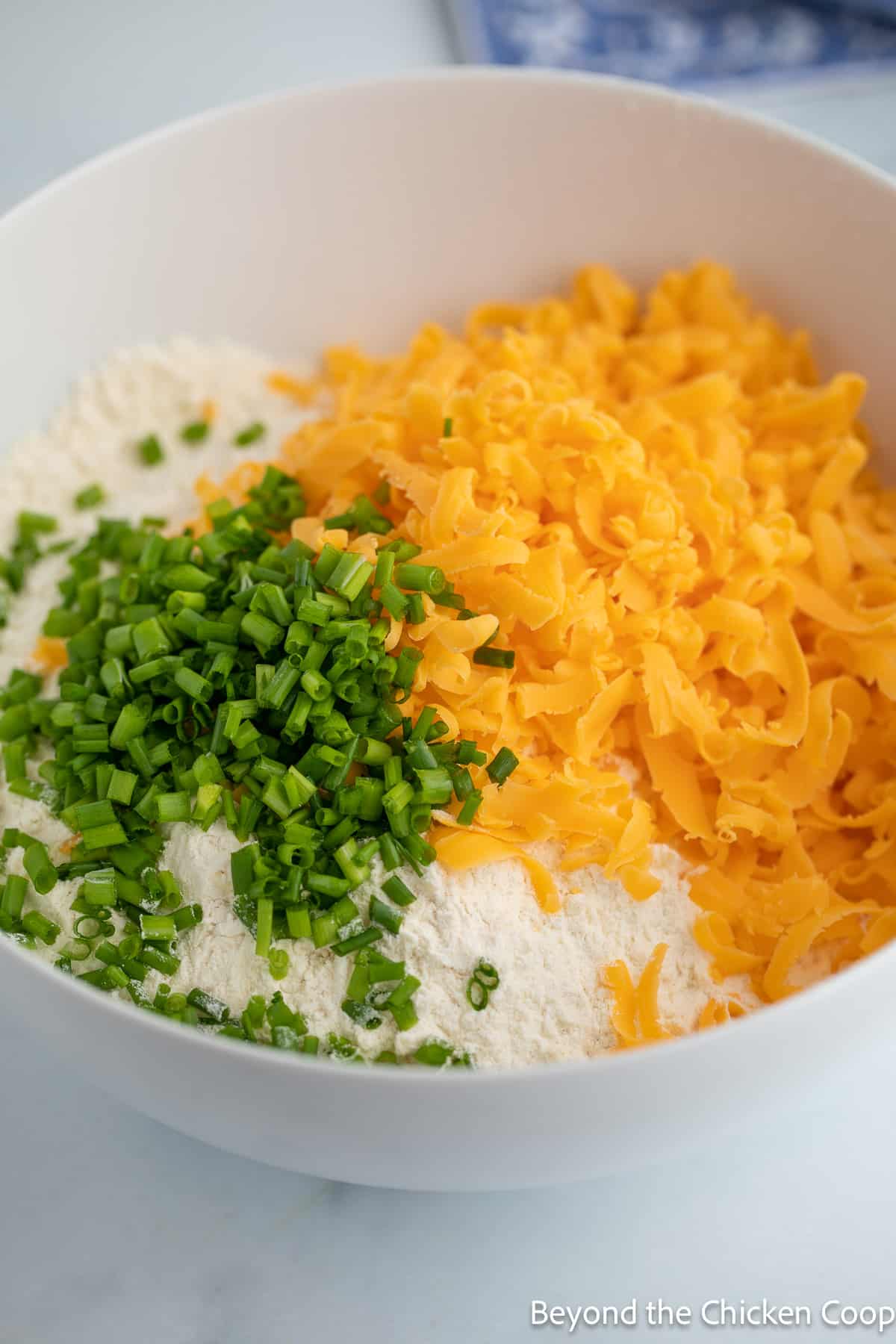 Shredded cheddar and chopped chives in a bowl with flour. 