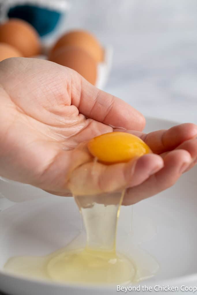 An uncooked egg in a hand with the whites falling off.