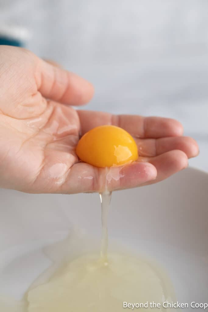 A yolk remaining in a hand with the whites in a bowl below the hand. 