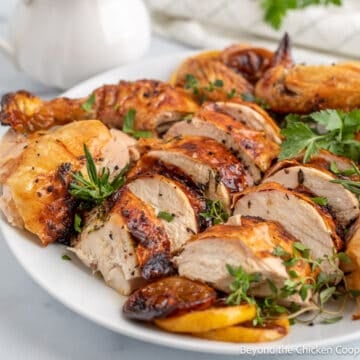 Sliced whole chicken arranged on a plate with lemon and herbs.