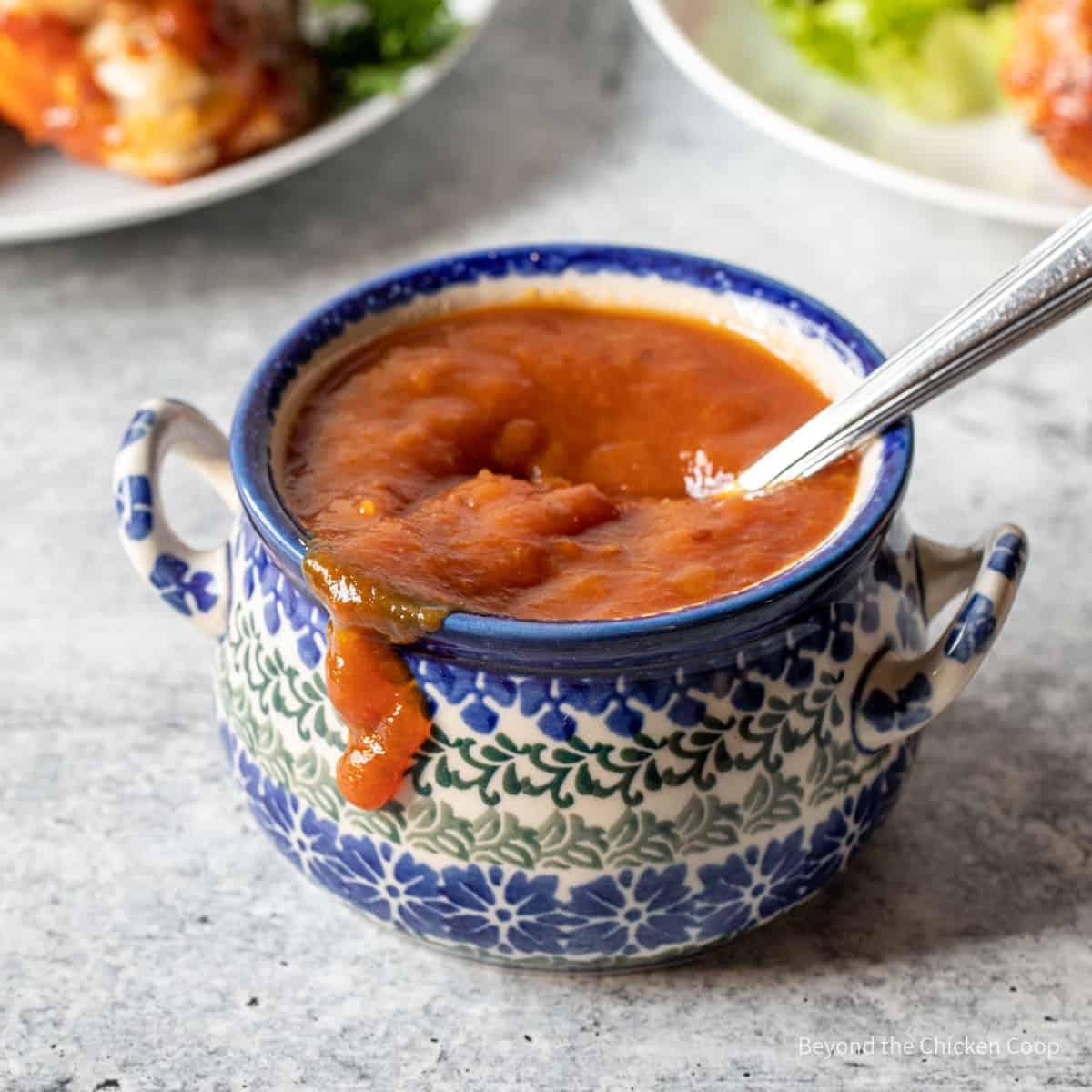 A small colorful crock filled with barbecue sauce. 