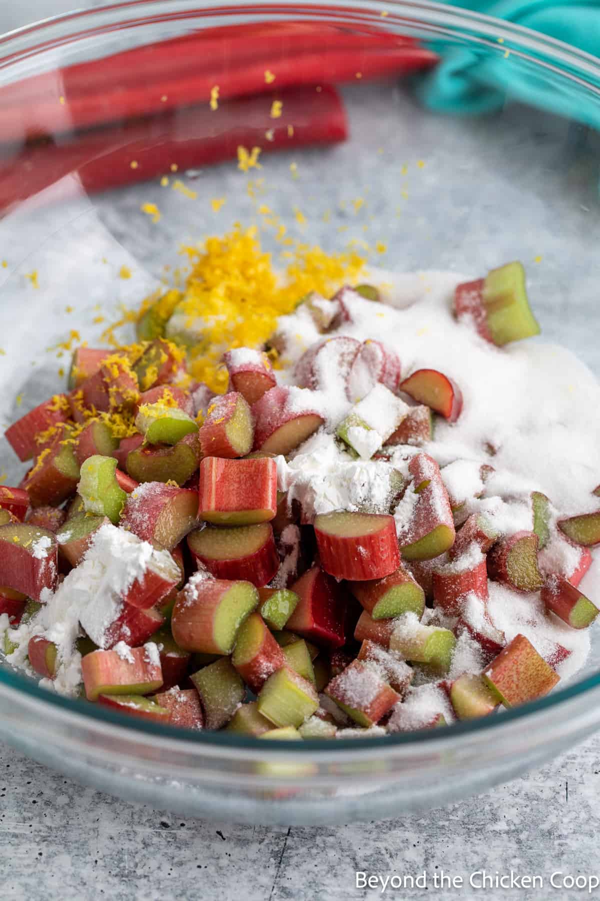 Chopped rhubarb with sugar and lemon zest in a mixing bowl. 