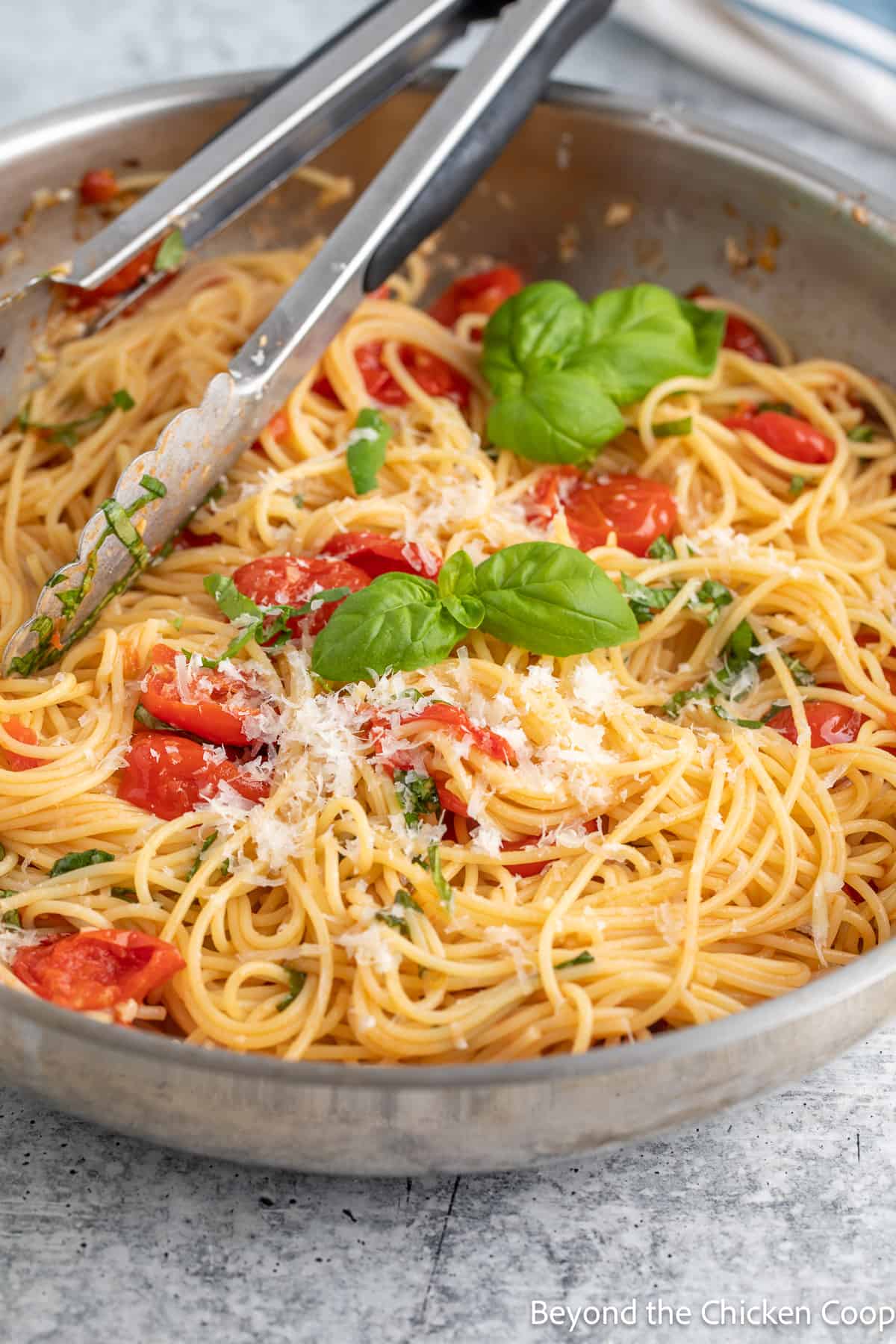 A pan filled with spaghetti noodles, tomatoes and basil. 