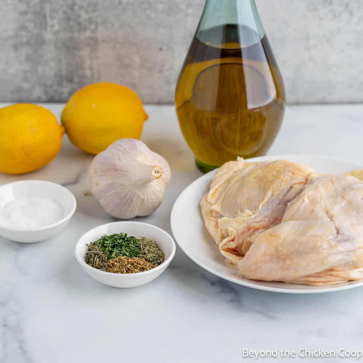 Chicken thighs, lemons, garlic and olive oil on a countertop. 