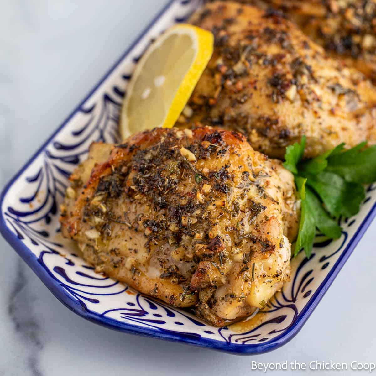 Baked Greek Chicken with sliced lemon on a colorful platter.
