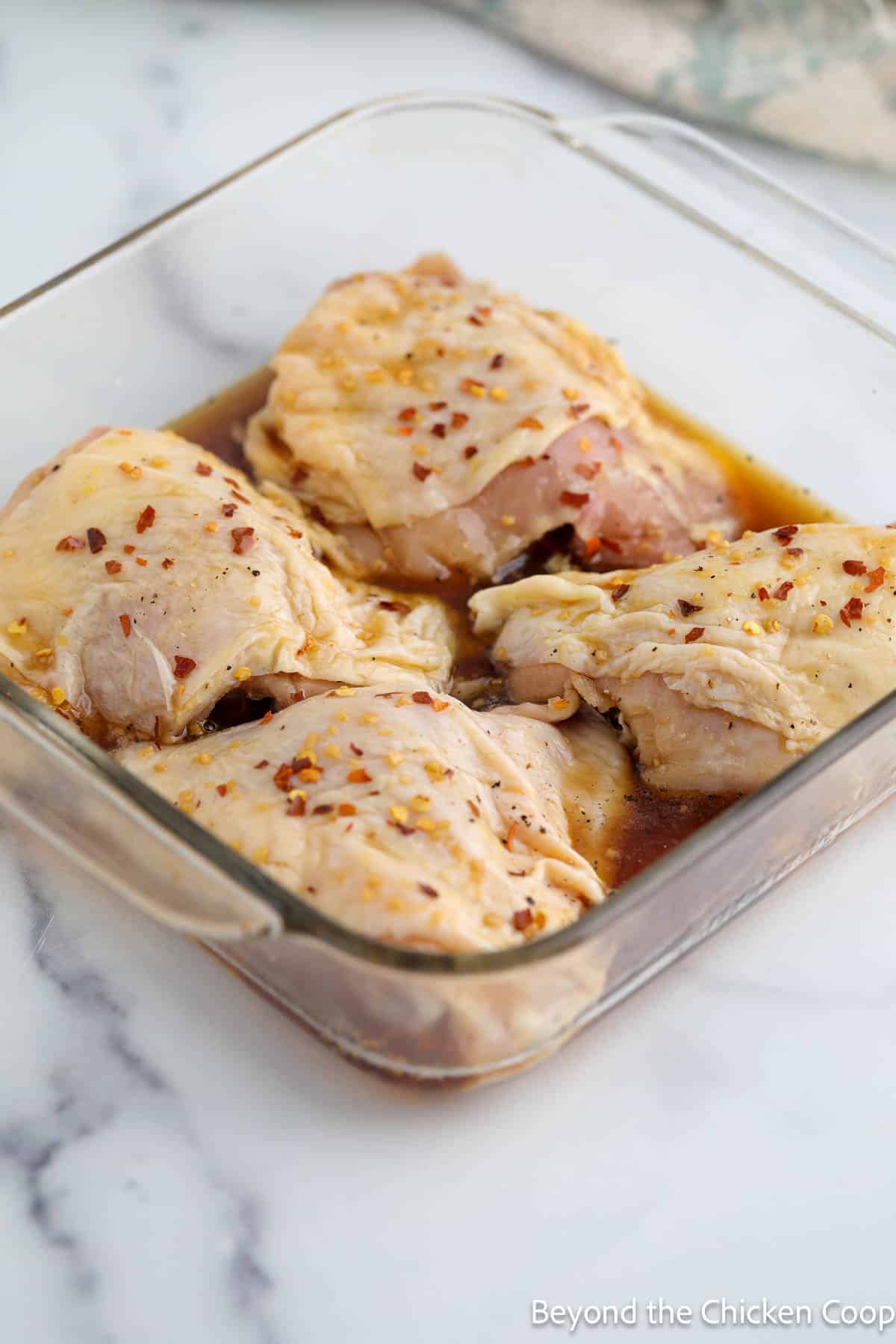 Raw chicken thighs covered in a sauce in a casserole dish. 