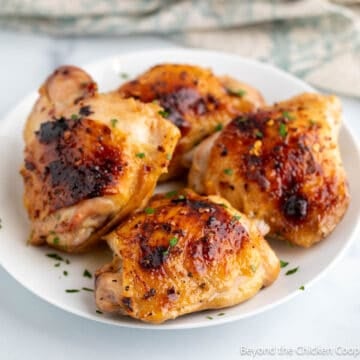 Cooked chicken thighs on a white plate.