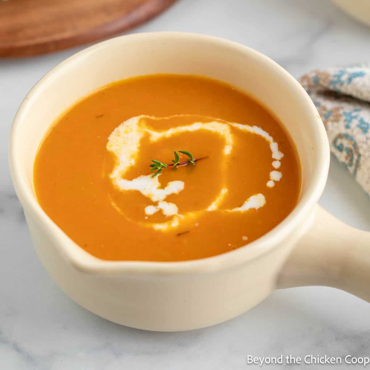 A cup of Butternut Squash Carrot Soup with a drizzle of cream on the top.
