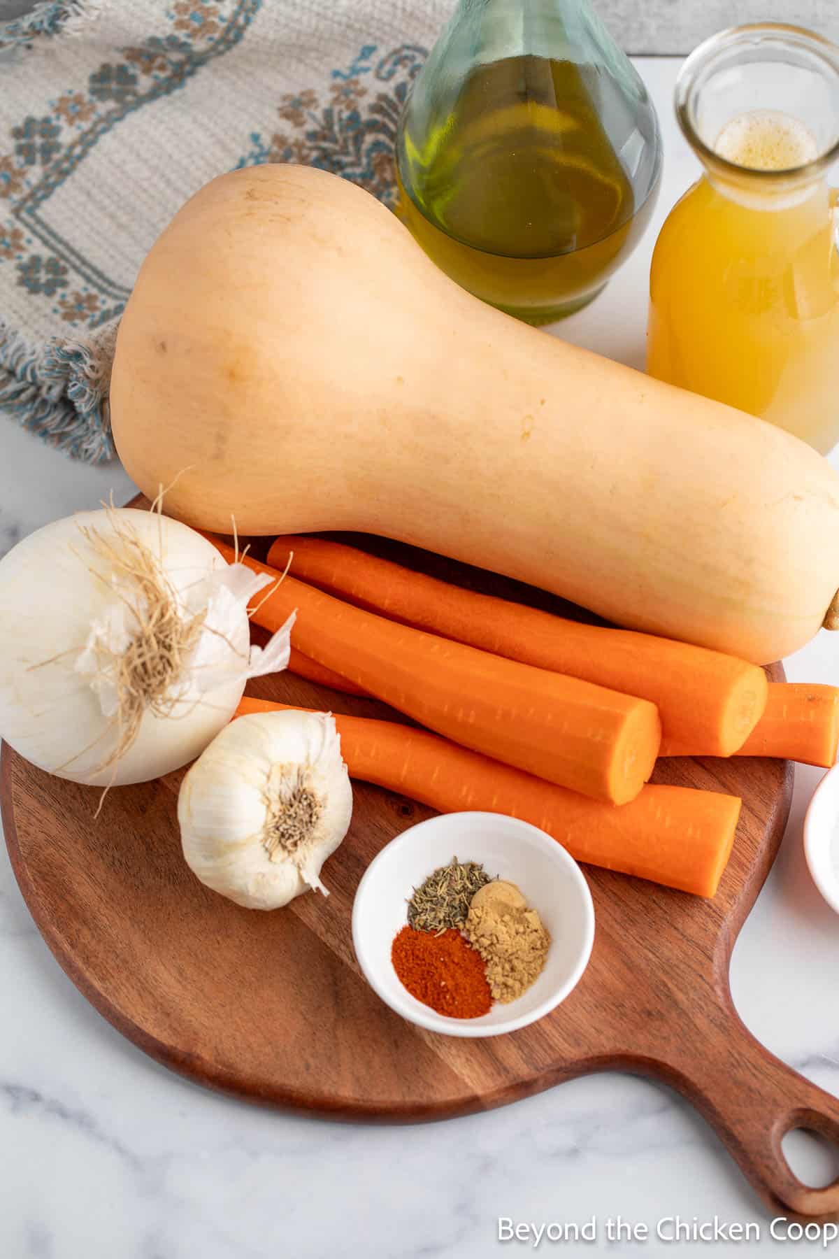 Butternut squash, carrots, onion, garlic and spices on a board.