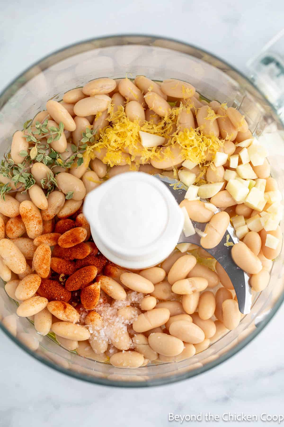 White beans, garlic and seasoning in a food processor bowl. 