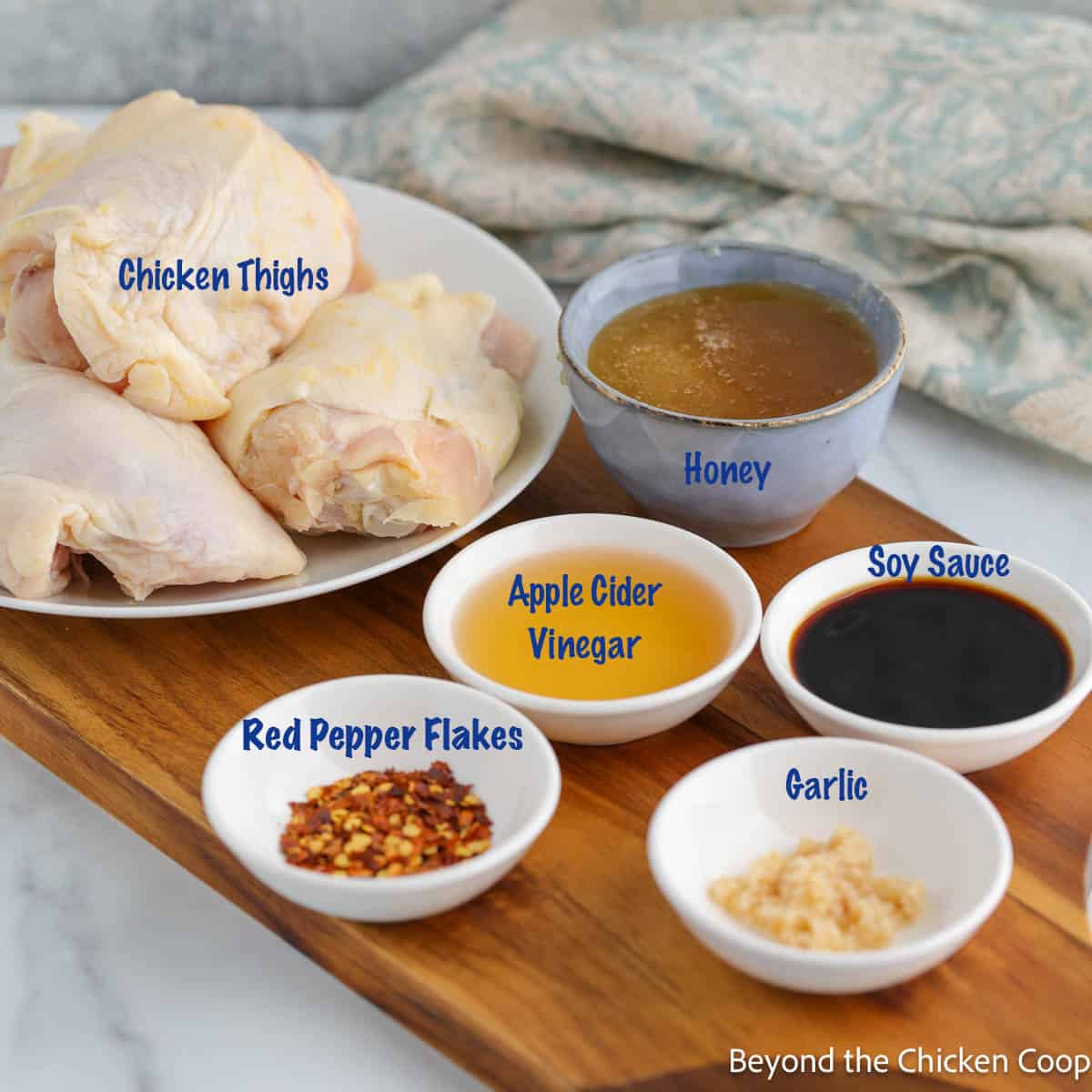 Chicken thighs and small bowls filled with seasoning on a wooden board. 