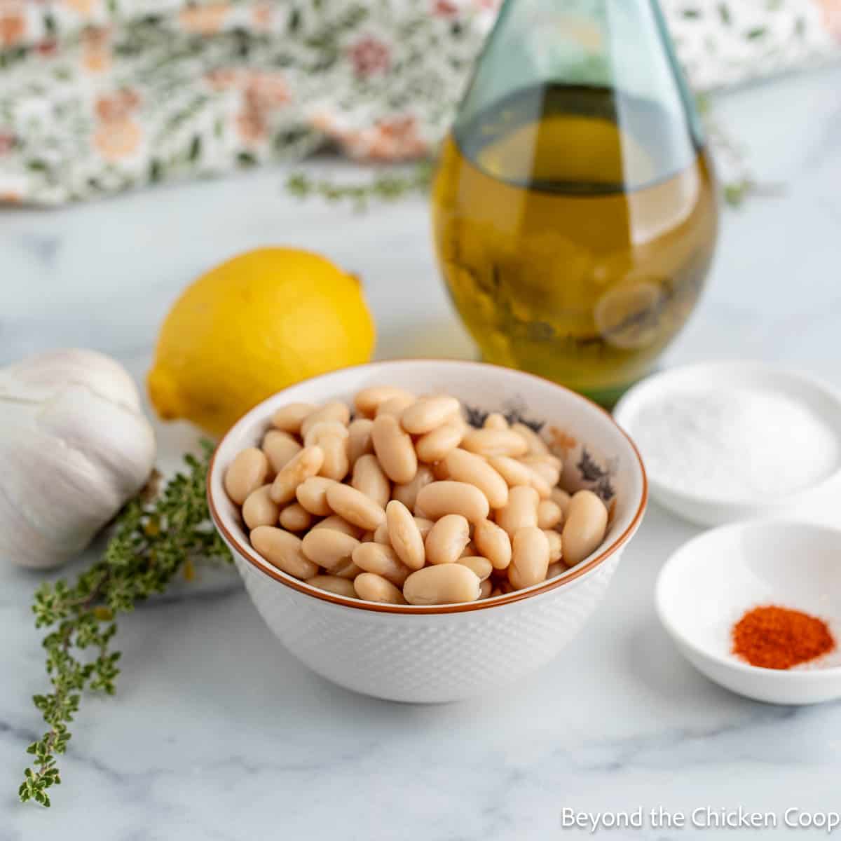 White beans in a small bowl next to a lemon and a bottle of olive oil. 