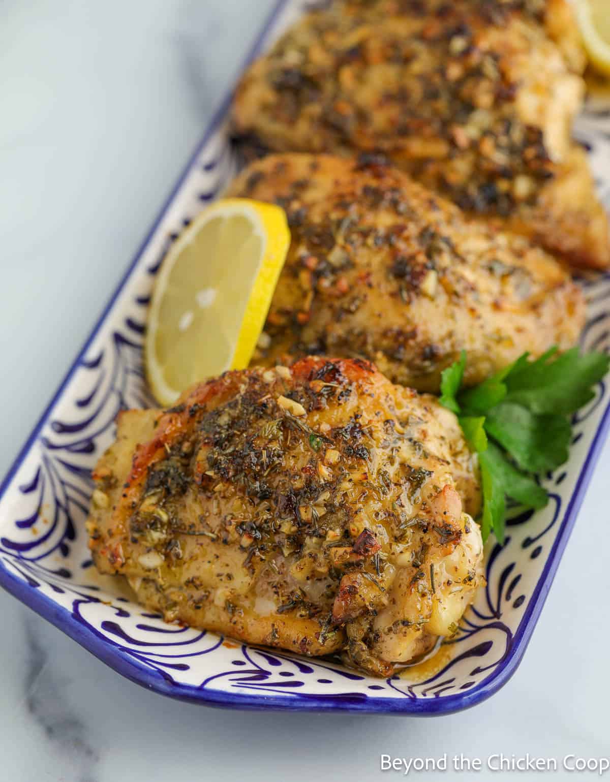 Greek chicken thighs on a blue and white platter.