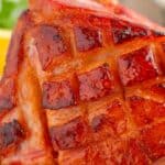 An orange glazed ham with score marks on the crust.