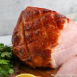 Orange glazed ham on a wooden board.