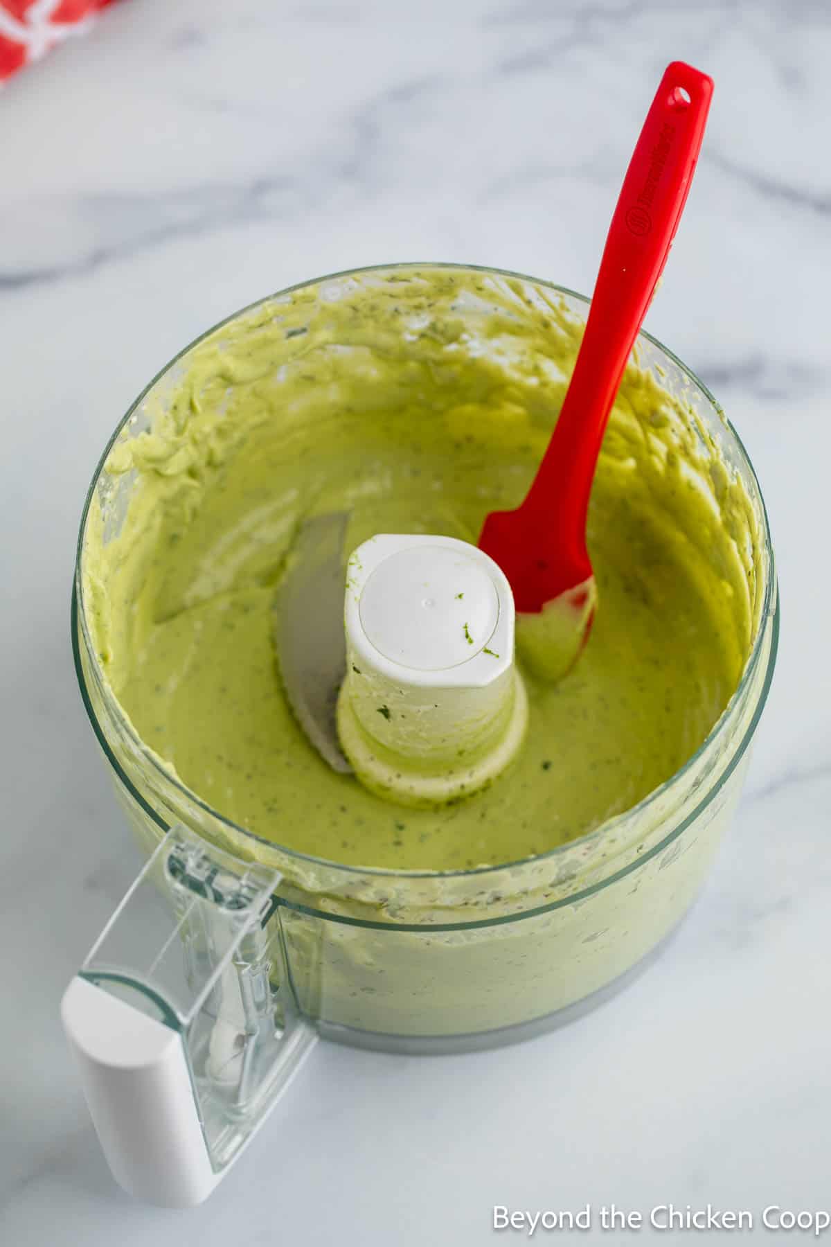 Avocado dressing in a food processor bowl with a red spatula. 