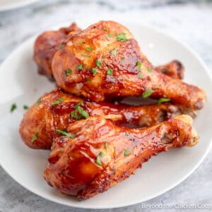 Baked BBQ Chicken Legs stacked on a white plate.