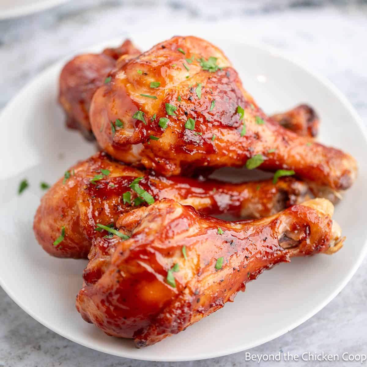 Baked BBQ Chicken Legs stacked on a white plate. 