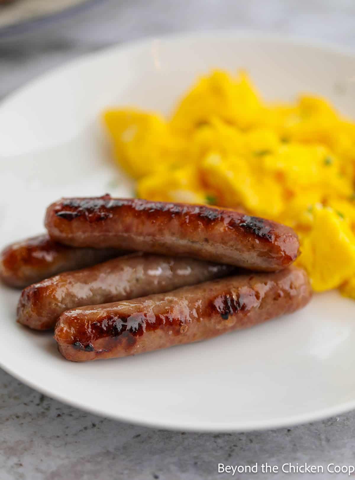 Sausage links and scrambled eggs on a white plate. 