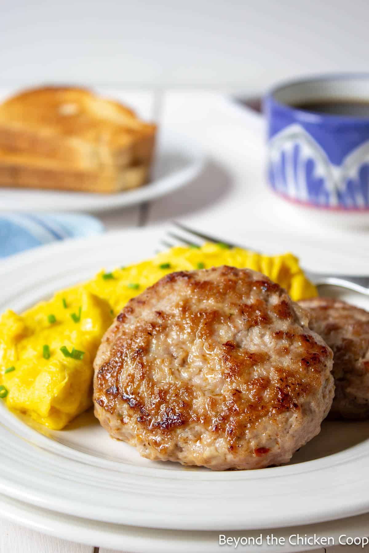 Breakfast sausage patties on a plate with scrambled eggs. 