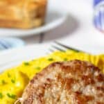 Pork sausage patty on a plate next to scrambled eggs.