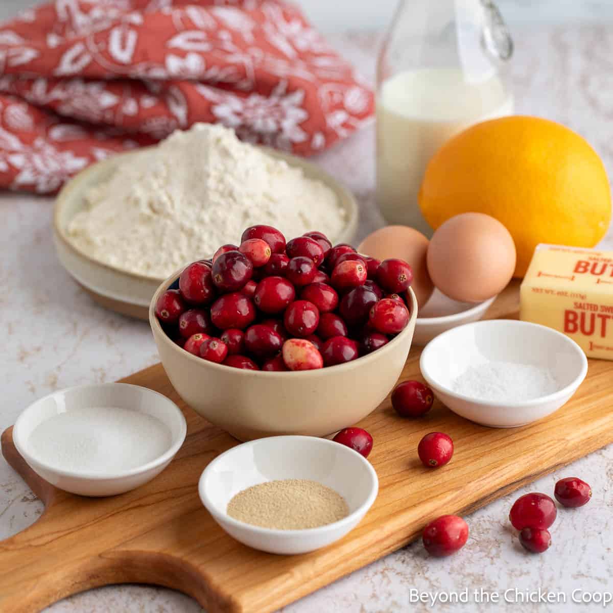 A bowl of cranberries next to small bowl of baking ingredients. 