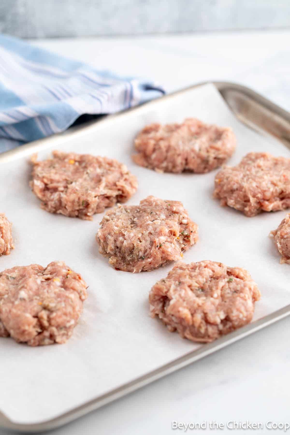 Uncooked breakfast sausage patties on a baking sheet. 