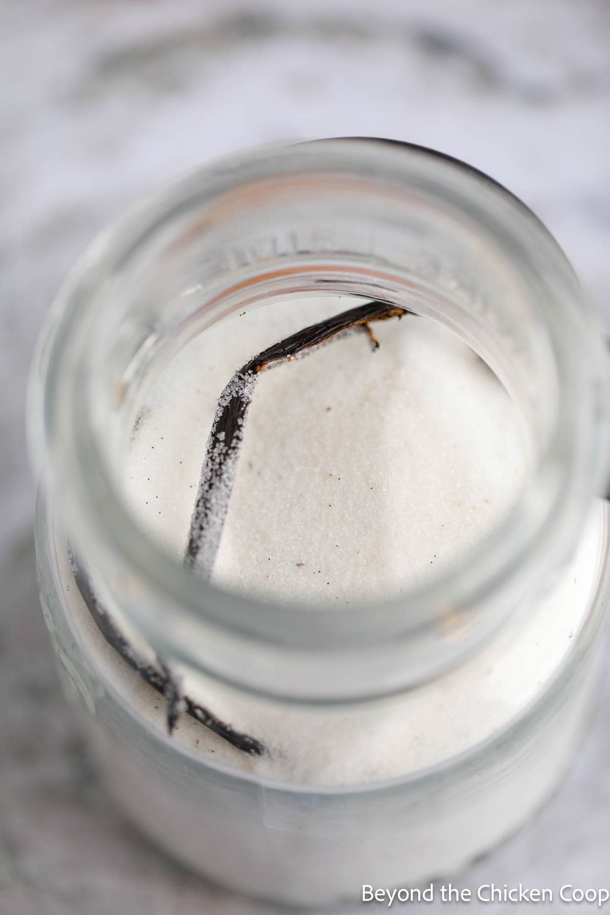 Adding sugar and a vanilla bean half to a glass jar. 