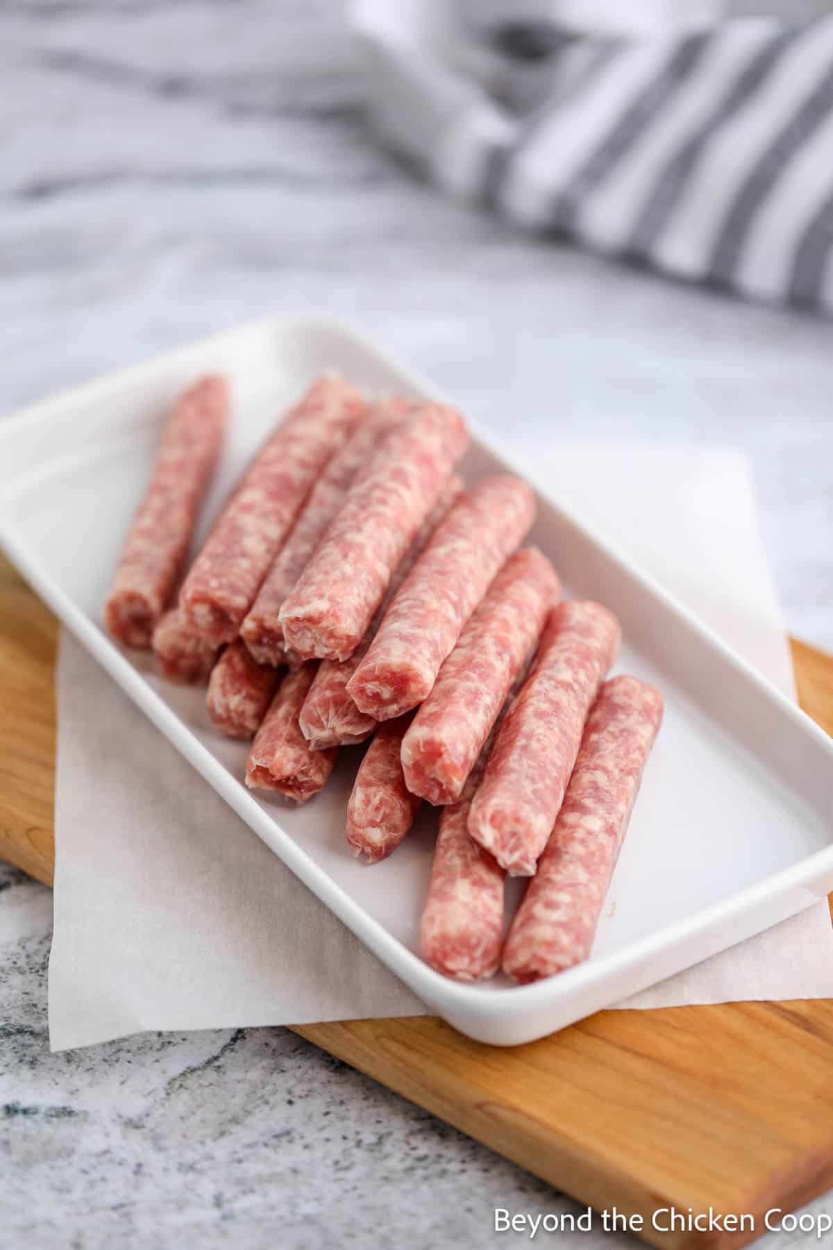 Uncooked breakfast sausage links on a white platter. 