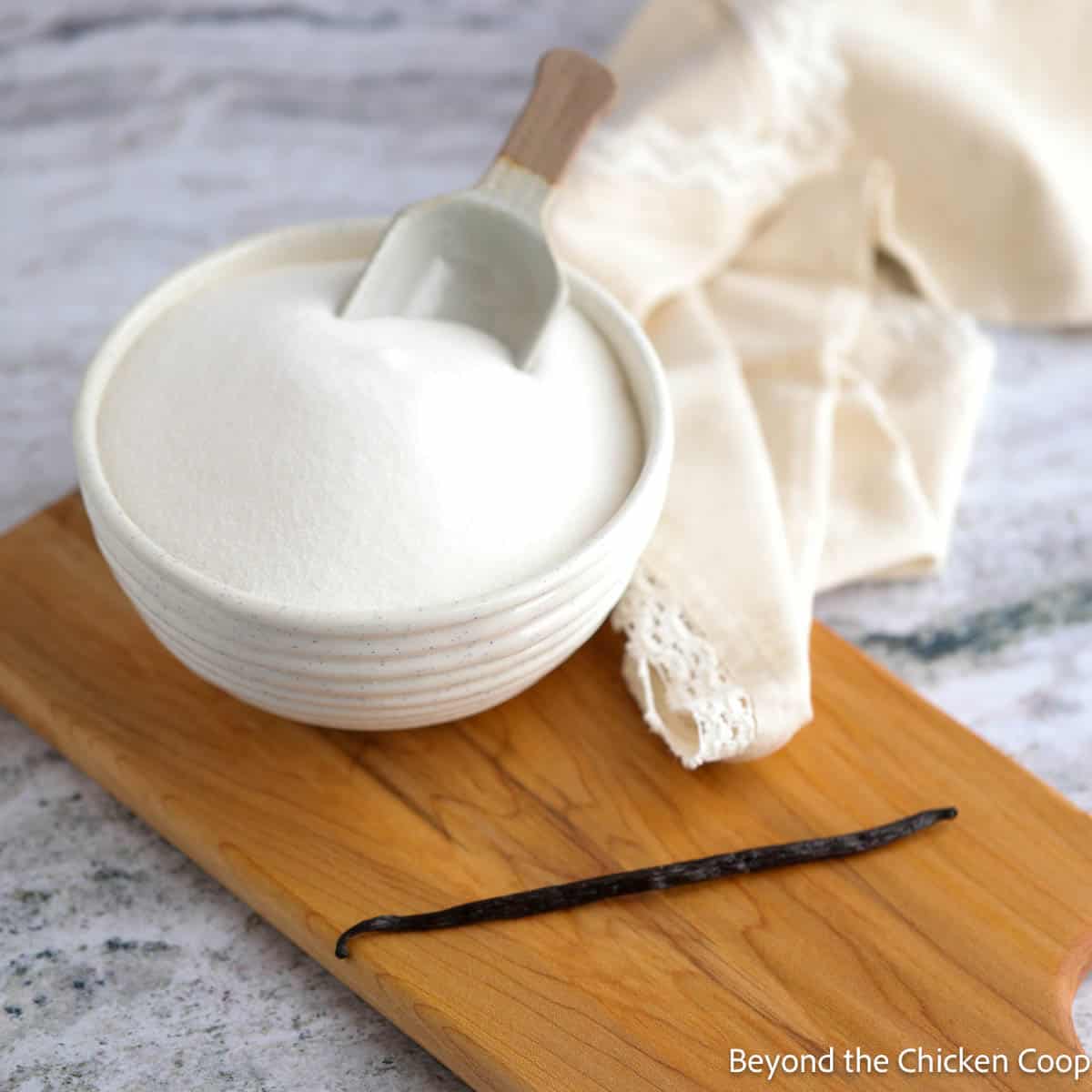 A bowl of sugar and a whole vanilla bean on a wooden board. 