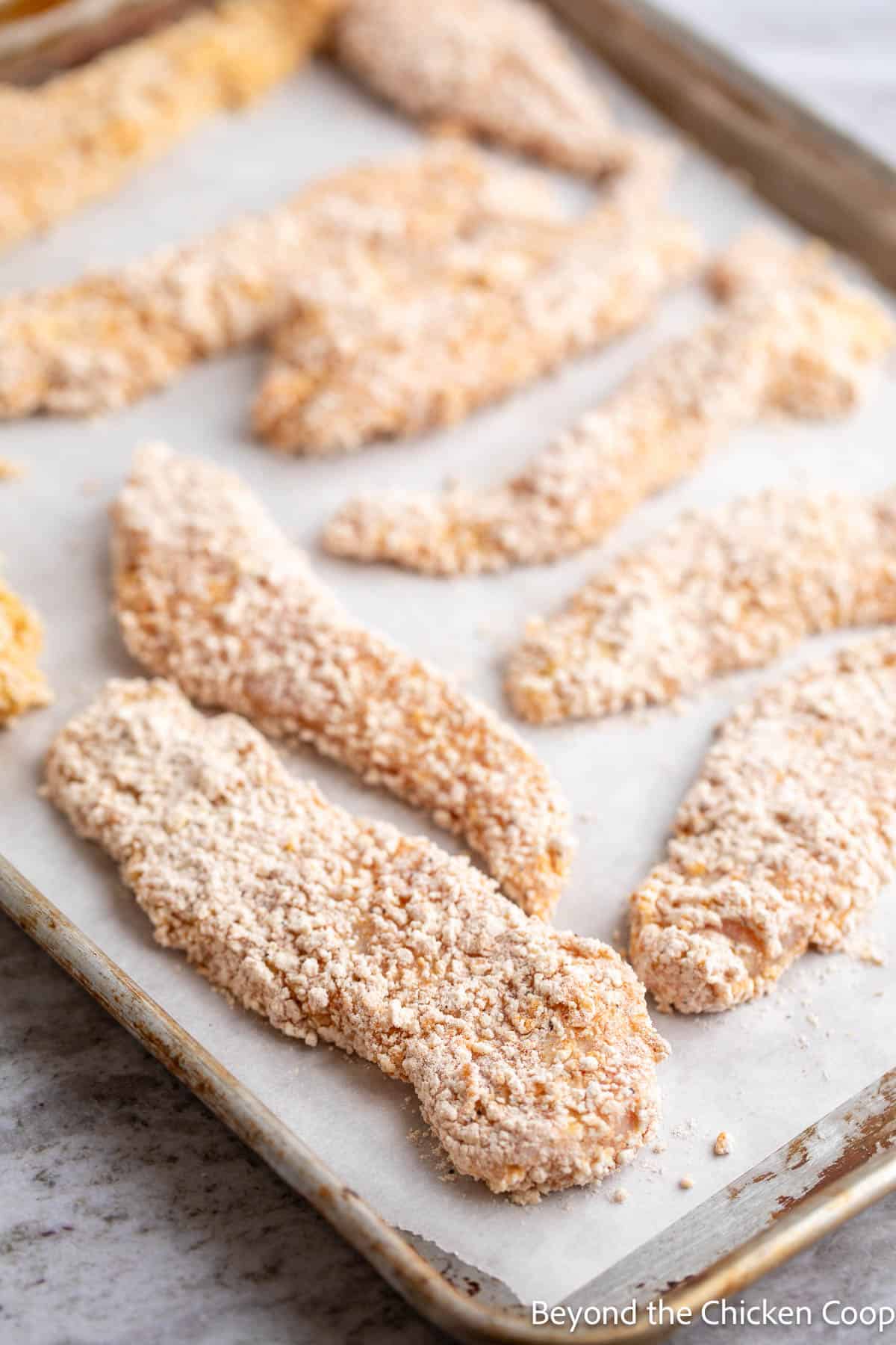 Battered chicken strips on a baking sheet. 